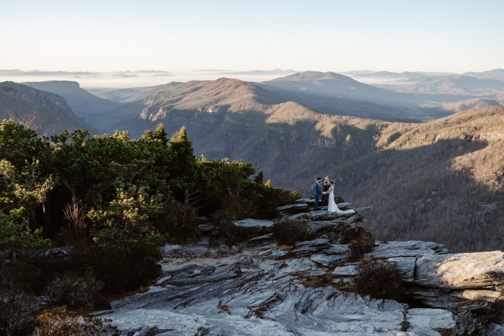 A couple standing on rocky outcropping with an officiant during their winter mountain elopement in Linville Gorge