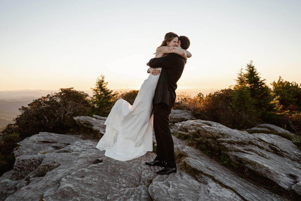 Groom lifting bride in an embrace after they eloped on a mountaintop